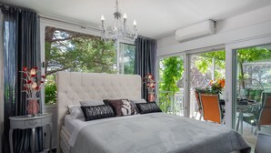 Un dormitorio con una cama grande, una araña, una mesita de noche y vistas al exterior.