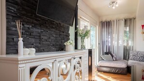 Una sala de estar con pared de piedra, un televisor de pantalla plana, una consola blanca y un sofá con cojines estampados.