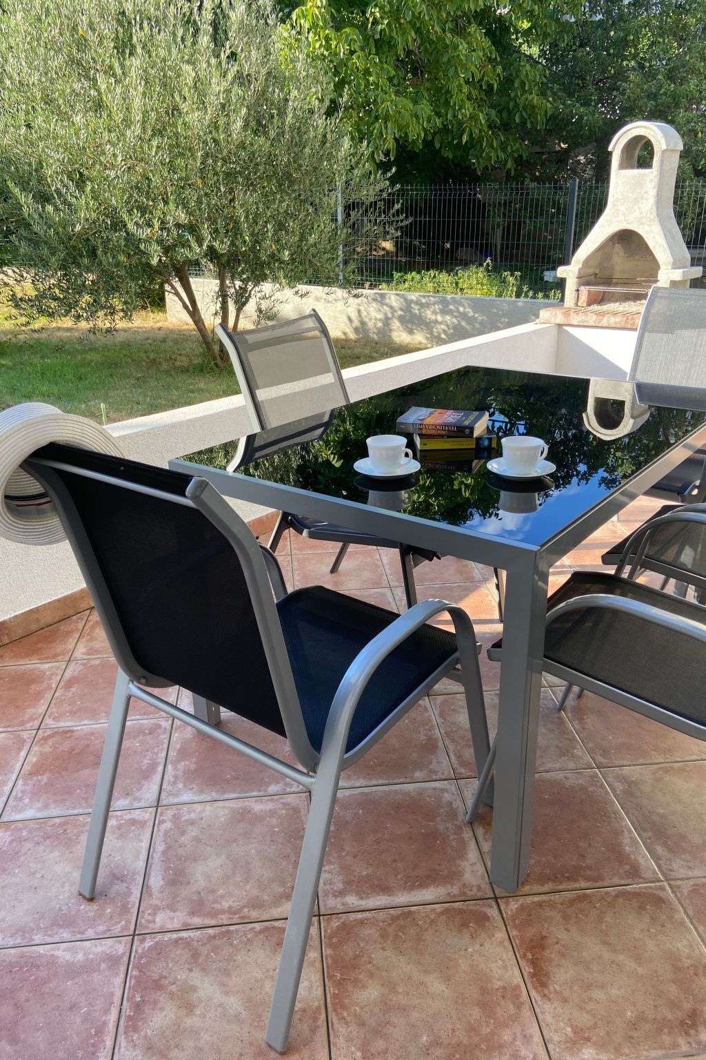 A glass-top outdoor table with chairs, a stone structure in the background, and a tiled patio.