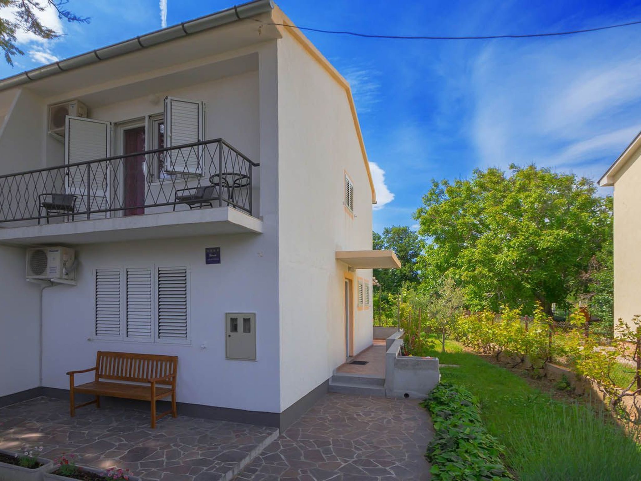 A two-story building with a balcony, a bench, and a small garden area.