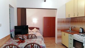 A compact hotel room with a bed, a TV, a dining table with chairs, a kitchenette with a stove and sink, and a wooden wardrobe. - Studio-Apartment mit Terrasse und Parkplatz by Interhome (Krk/Baška)