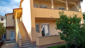 A two-story building with a staircase leading to the entrance, a balcony on the upper floor, and a small garden area with a tree and potted plants. - Studio-Apartment mit Terrasse und Parkplatz by Interhome (Krk/Baška)