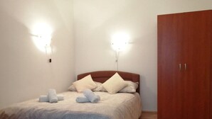 A bedroom with a bed, two wall-mounted lights, a wooden wardrobe, and neatly folded towels on the bed. - Studio-Apartment mit Terrasse und Parkplatz by Interhome (Krk/Baška)