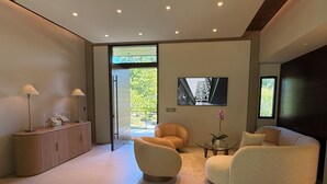 A modern living room with a sofa, armchair, and a glass coffee table. There is a TV mounted on the wall and a cabinet with a lamp. - Executive Luxury Ritz Level Spa Oasis

IncludesEQS Mercedes or Tesla

Private (Charlotte)