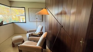Una camera moderna con un pannello curvo in legno, un'ampia finestra vista alberi e una lampada da terra.