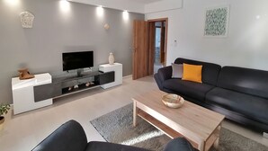 Una sala de estar moderna con un televisor de pantalla plana, un sofá de cuero negro, una mesa de centro de madera y una alfombra gris.