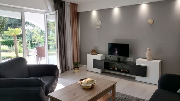 Una sala de estar moderna con un televisor de pantalla plana sobre un soporte negro, una mesa de centro de madera y dos sofás negros.