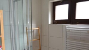 Un bagno con cabina doccia in vetro, una sedia di legno, un termosifone e una finestra con tende.