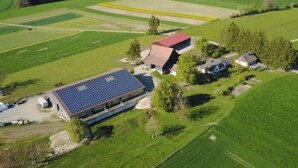 Vista aerea di una proprietà rurale con un ampio impianto di pannelli solari, una casa colonica e campi circostanti.