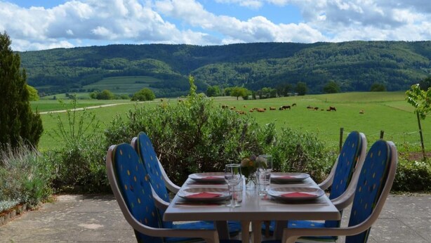 Tavolo apparecchiato per due con vista su un campo verde e delle colline sullo sfondo.