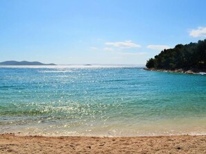 Una playa con agua turquesa cristalina, una orilla de arena y un área boscosa al fondo.
