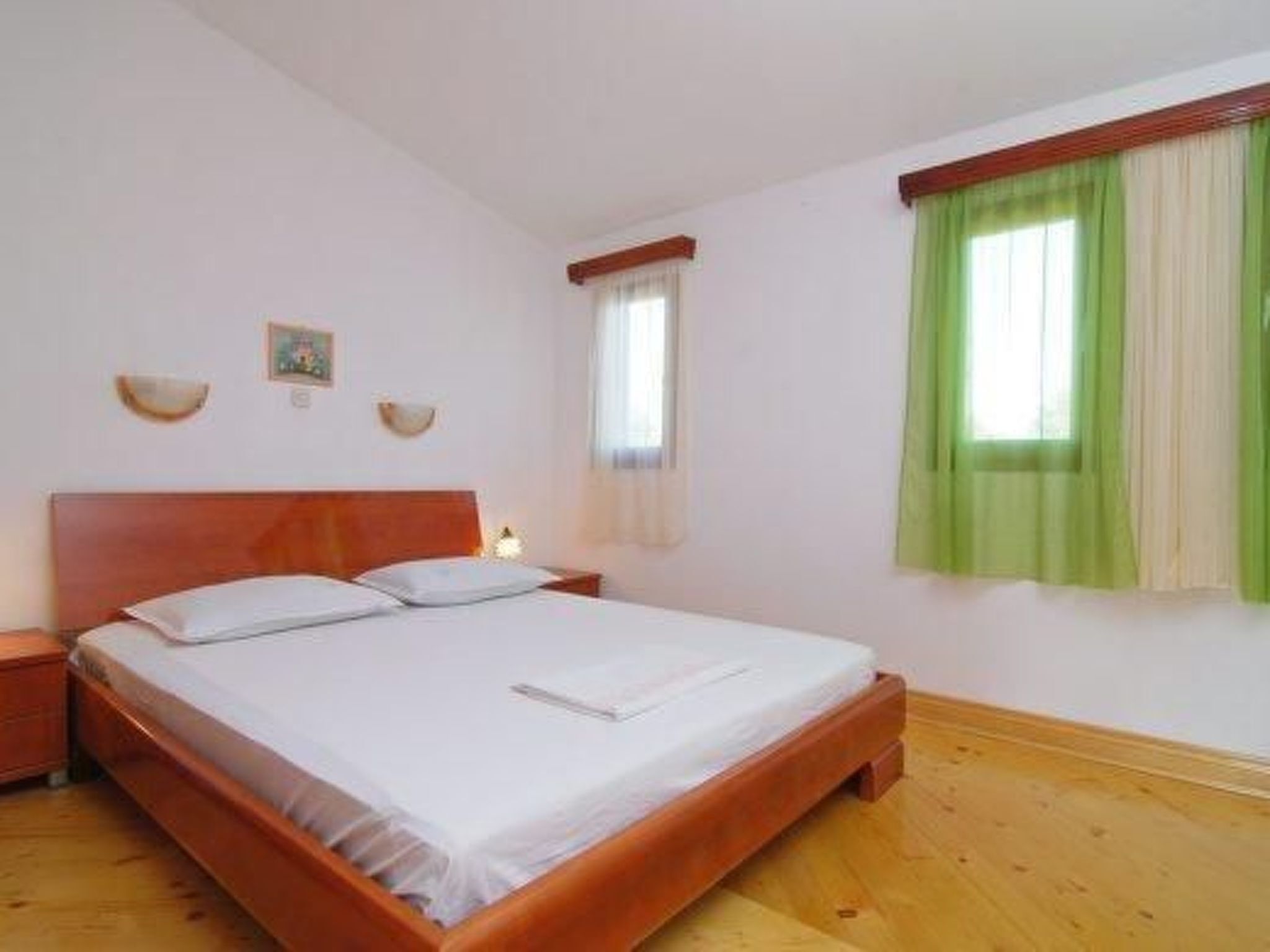 A single bed with a wooden headboard, a nightstand, and a window with green curtains.