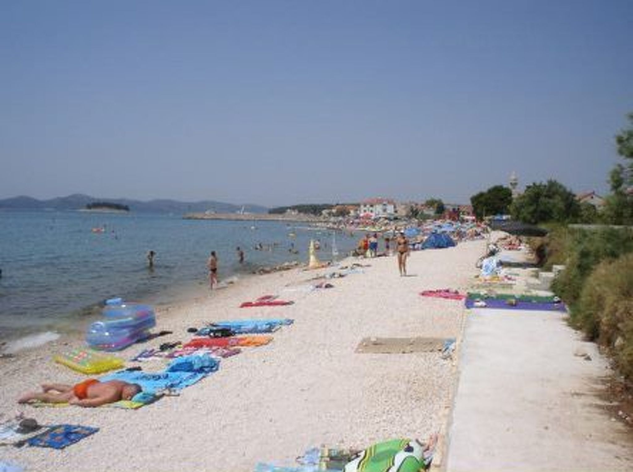 Une plage où l’on peut voir des gens bronzer et se baigner, avec des parasols et des chaises de plage.