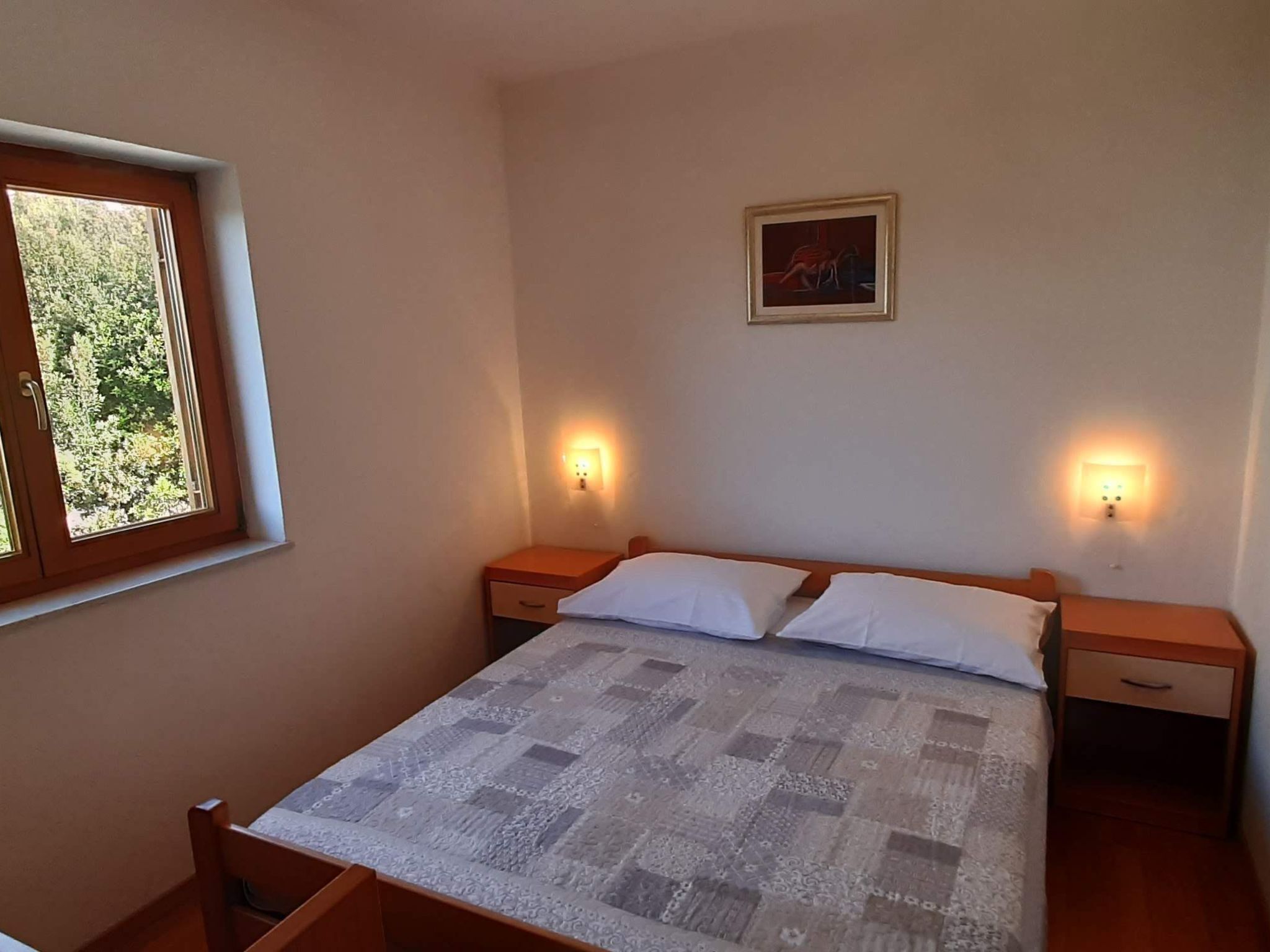 A bedroom with a bed, two bedside tables, a window, and a wall-mounted light fixture.