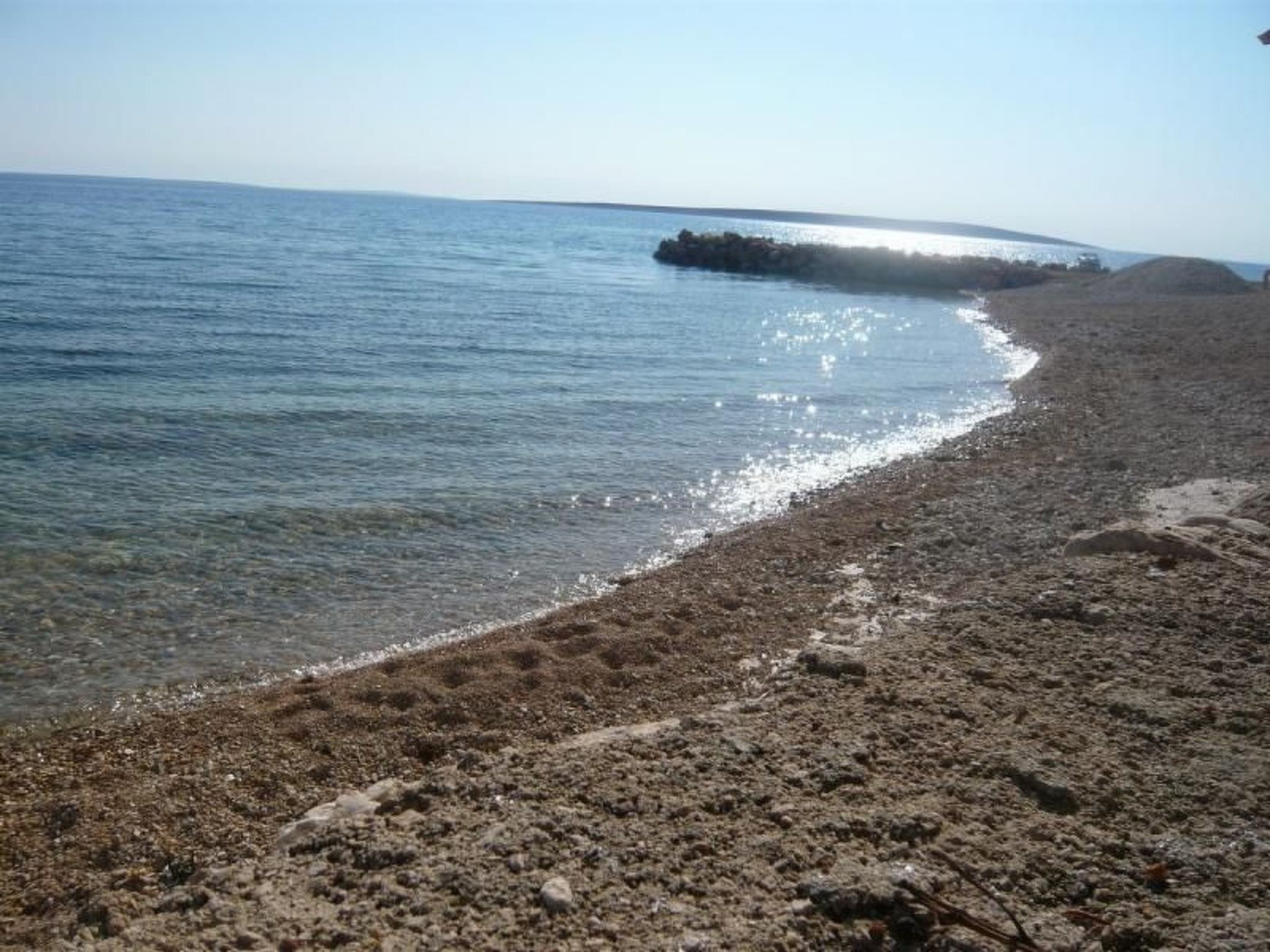 A beach with clear water, a rocky shoreline, and a distant landmass.