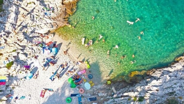 Vue aérienne d’une plage aux eaux turquoise et limpides, bordée de falaises rocheuses et parsemée d’objets divers.