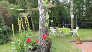 Ein Garten mit Baumstumpf, roten Blumen und einem Tisch mit Stühlen unter einer Markise.