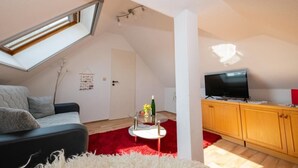 Ein gemütliches Schlafzimmer im Loft-Stil mit schrägem Dach, einem Bett, einem Fernseher und einer kleinen Essecke.