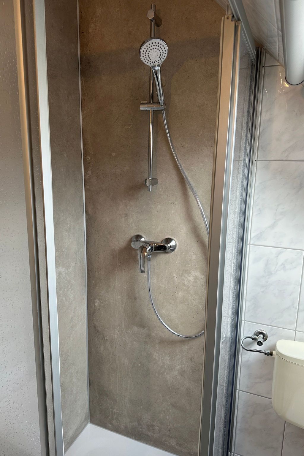 A shower with a handheld showerhead and a wall-mounted faucet.