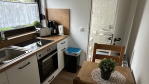 Een compacte keuken met een fornuis, wastafel en een klein eethoekje met een tafel en stoel.