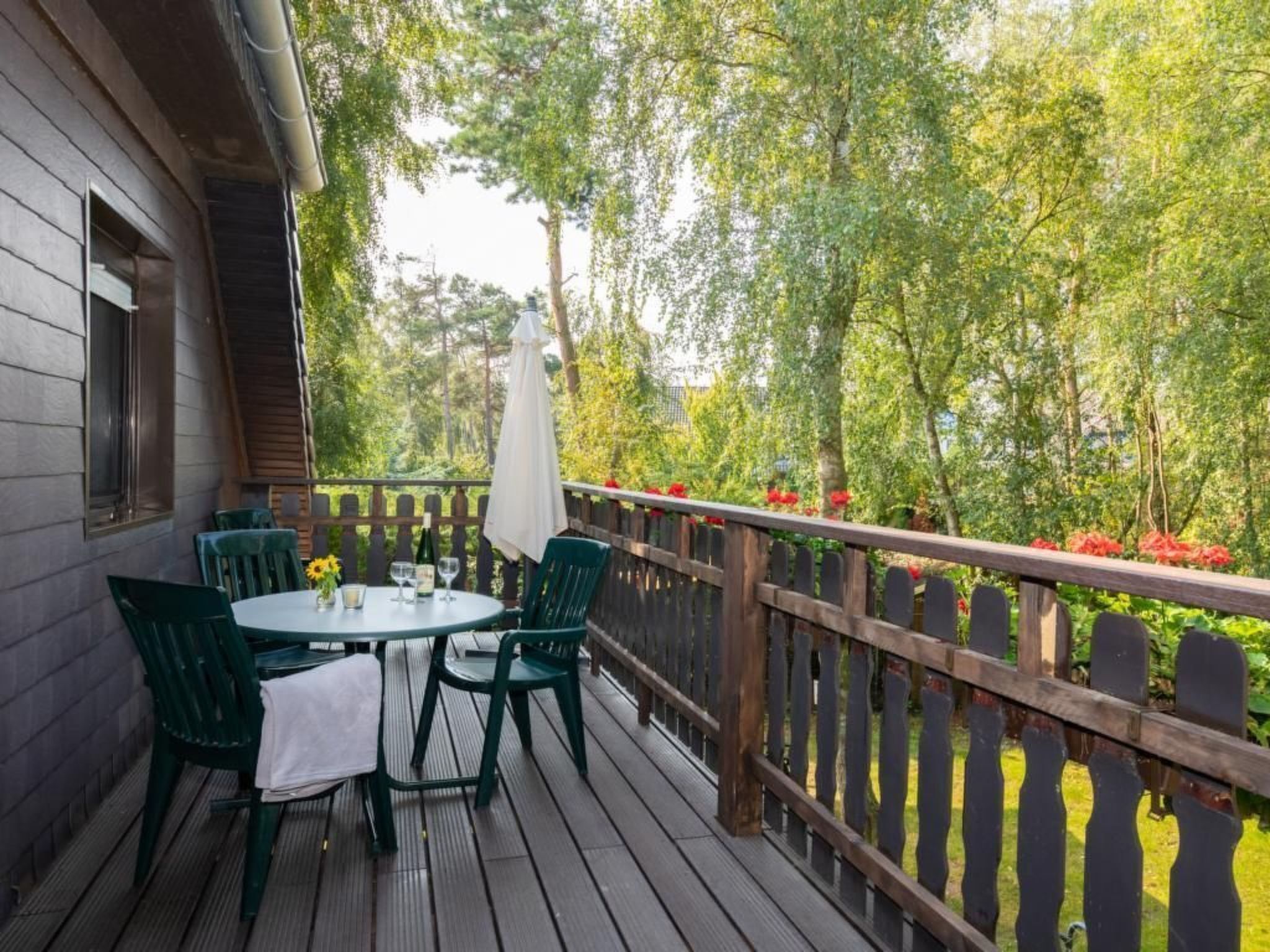 A wooden deck with a table and chairs, surrounded by a wooden fence and lush greenery.