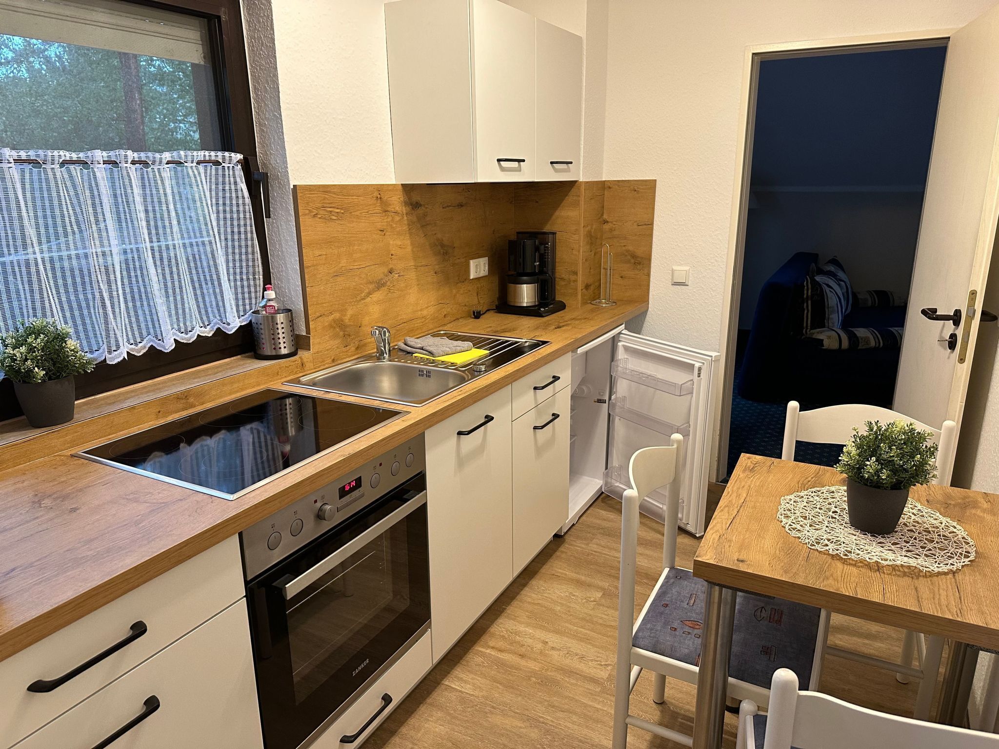 Een compacte keuken met een ingebouwde oven, een spoelbak en een klein eethoekje met een tafel en stoelen.
