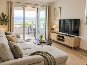 Ein Wohnzimmer mit Sofa, Fernseher und einem Balkon mit Aussicht.