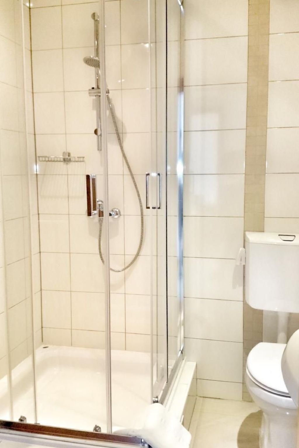 A glass-enclosed shower with a handheld showerhead and a handheld shower attachment.