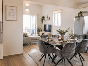 Ein moderner Essbereich mit Tisch für vier Personen, einer Couch und einem Fernseher im Hintergrund.