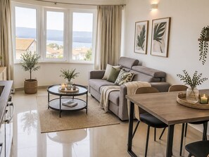 Ein Wohnzimmer mit Sofa, Couchtisch, Esstisch und Stühlen sowie Blick ins Freie.
