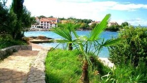 A stone pathway leading to a coastal area with lush greenery and a view of buildings across the water. - mit Blick auf das Wasser by Interhome (Krk/Milohnići)