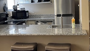 A modern kitchen with granite countertops, stainless steel appliances, and a bar area with stools. - Remodeled studio in the heart of  historic downtown Durango! (Durango)