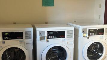 Three stacked front-loading washing machines in a laundry room with a green sign on the wall.