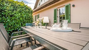 A wooden deck with outdoor furniture, a table set with white teacups and a vase, and a building with green shutters and a thatched roof. - Schwanke´s Feri by Interhome (Gingst)