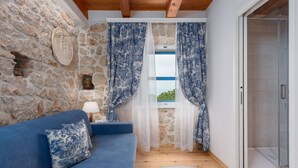 A room with a stone wall, a wooden ceiling, a blue sofa, and a view through sheer curtains to a balcony. - "VillaTonka auf der Insel Krk, Malinska" by Interhome (Krk/Milohnići)