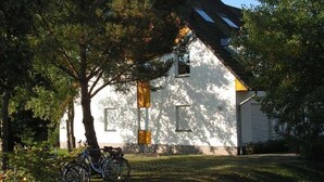 Una casa blanca con techo inclinado, una bicicleta estacionada al frente y un árbol a la izquierda.