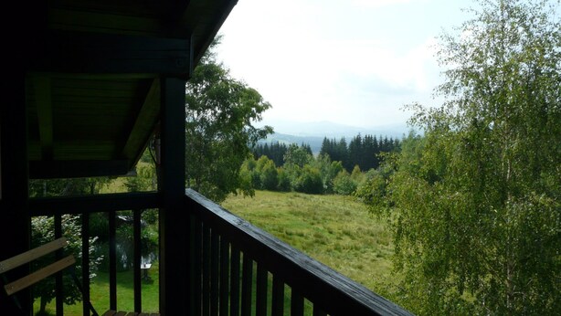Een houten terras met een bankje, met uitzicht op een grasveld met bomen en een verafgelegen bergketen.