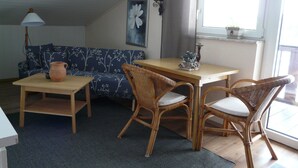 Een gezellige woonkamer met een bank, twee rotan fauteuils, een bijzettafeltje en een lamp.