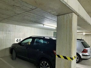 Un parcheggio sotterraneo con pareti in cemento, un'auto parcheggiata in uno stallo contrassegnato dal numero 46 e nastro di sicurezza giallo vicino a un pilastro.