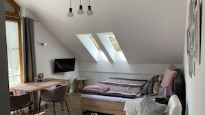 A loft-style bedroom with a sloped ceiling, skylights, a bed, a sofa, a TV, and a dining area with a table and chairs. - Appartement in Langfurth mit Kleinem Balkon by Interhome (Langfurth)
