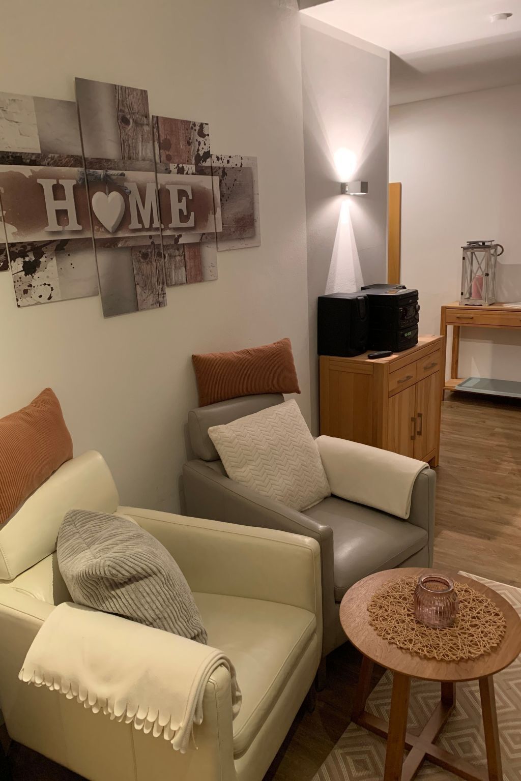 Un salon comprenant un canapé, une petite table ronde, un meuble et un luminaire fixé au mur.