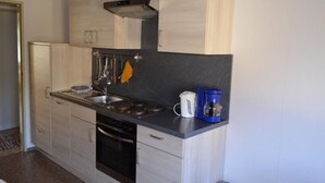 Uma cozinha moderna com armários de madeira clara, bancada preta, eletrodomésticos de aço inoxidável e uma cafeteira.