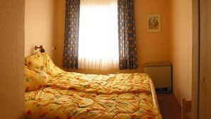Um quarto pequeno e acolhedor com uma cama de solteiro, um radiador e uma janela com cortinas.