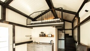 Una cocina compacta con una isla central, una zona de comedor con un sofá de cuero negro y una escalera que conduce a un nivel superior.