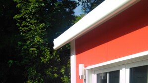 Un patio con una mesa, sillas, un ventanal corredero y fachada de un edificio rojo.