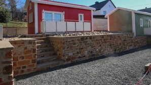Una hilera de edificios pequeños de una sola planta, con un muro de piedra en primer plano.