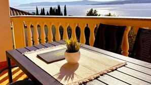 En balkon med udsigt til hav og bjerge, et bord med en plante og en bog.