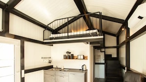 A compact kitchen with a central island, a dining area with a black leather sofa, and a staircase leading to an upper level. - mit Grill in Bad Marienberg by Interhome (Bad Marienberg)