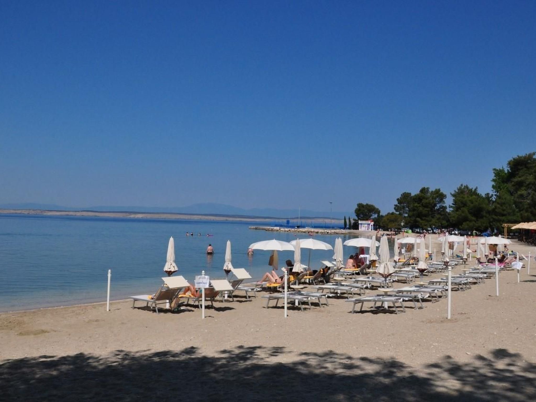 Ein Strand mit Reihen von Liegestühlen und Sonnenschirmen, einem klaren Himmel und ruhigem Wasser.