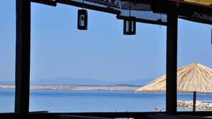 Vista a la playa desde un área de estar techada, con una sombrilla de paja y farolillos colgantes.